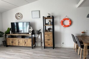 Un salon moderne avec un téléviseur à écran plat, des meubles en bois, une bibliothèque, une horloge murale et un objet décoratif en forme de bouée de sauvetage.