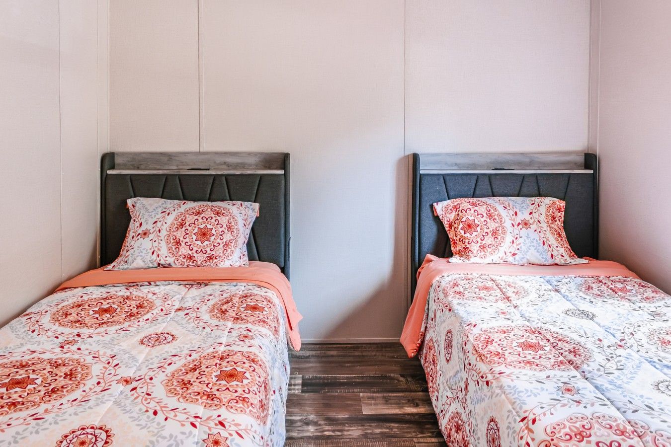 Two single beds with headboards, a wooden floor, and a plain wall.