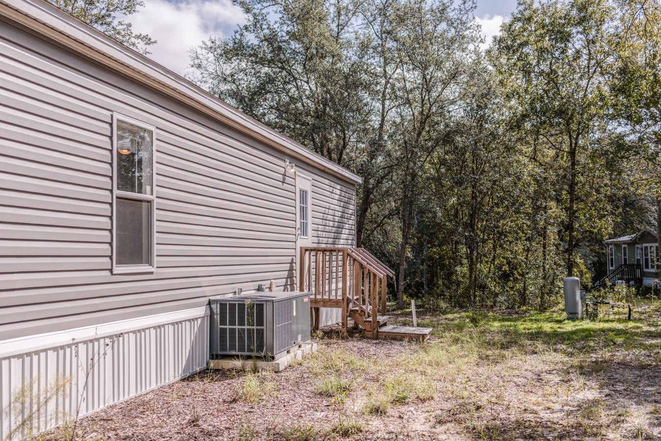 A single-story house with a wooden deck, an air conditioning unit, and a fenced yard.