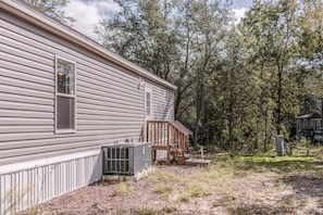 A single-story house with a wooden deck, an air conditioning unit, and a fenced yard.