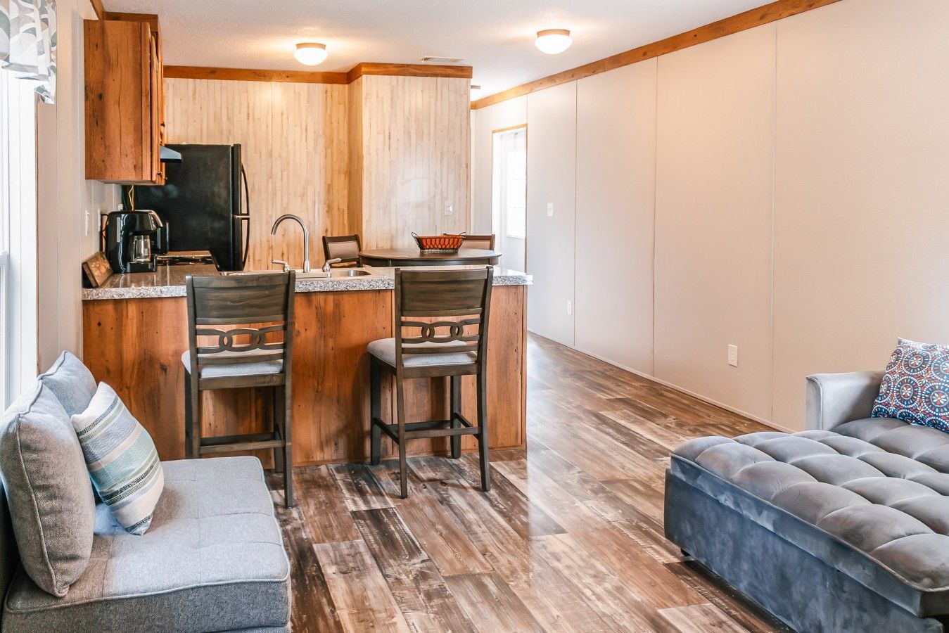 A compact living space with a kitchenette, two bar stools, a sofa, and a cushioned bench.