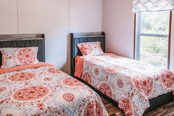 Two twin beds with matching headboards and floral bedding, positioned next to a window with a view of greenery.