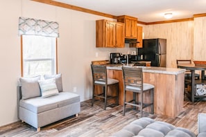 A compact kitchen with wooden cabinets, a black refrigerator, and a bar area with stools.