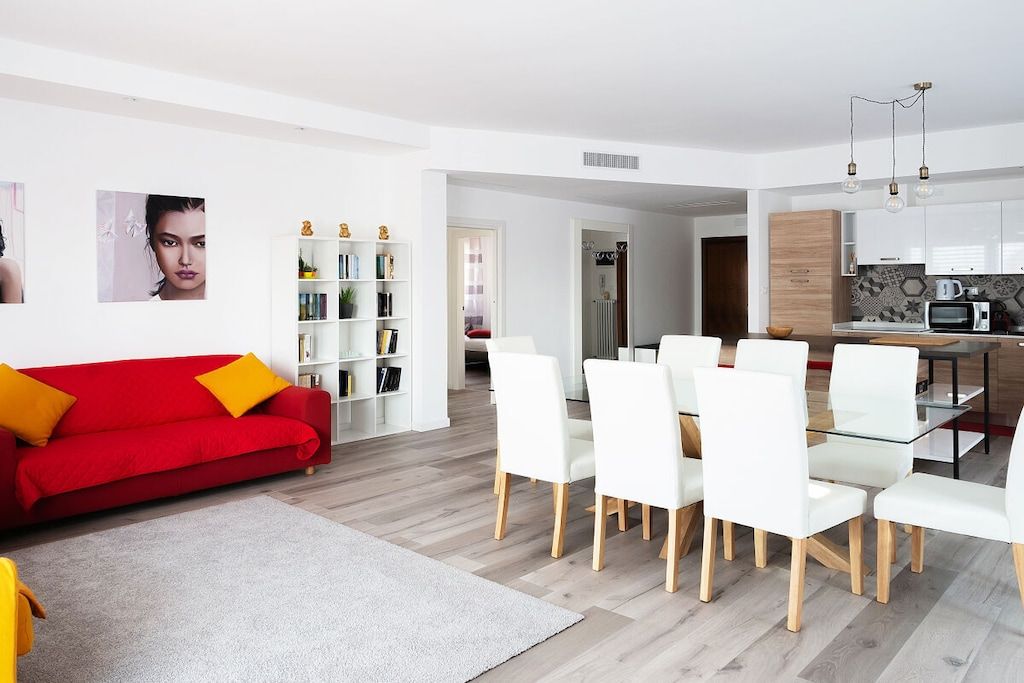 Ein modernes Wohnzimmer mit einem roten Sofa, weißen Esstühlen und einem Glastisch.