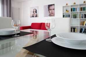 A modern living room with a glass table, two wine glasses, a red sofa, and a bookshelf with books and decorative items. - Residenza Conte Manetti (Mira)