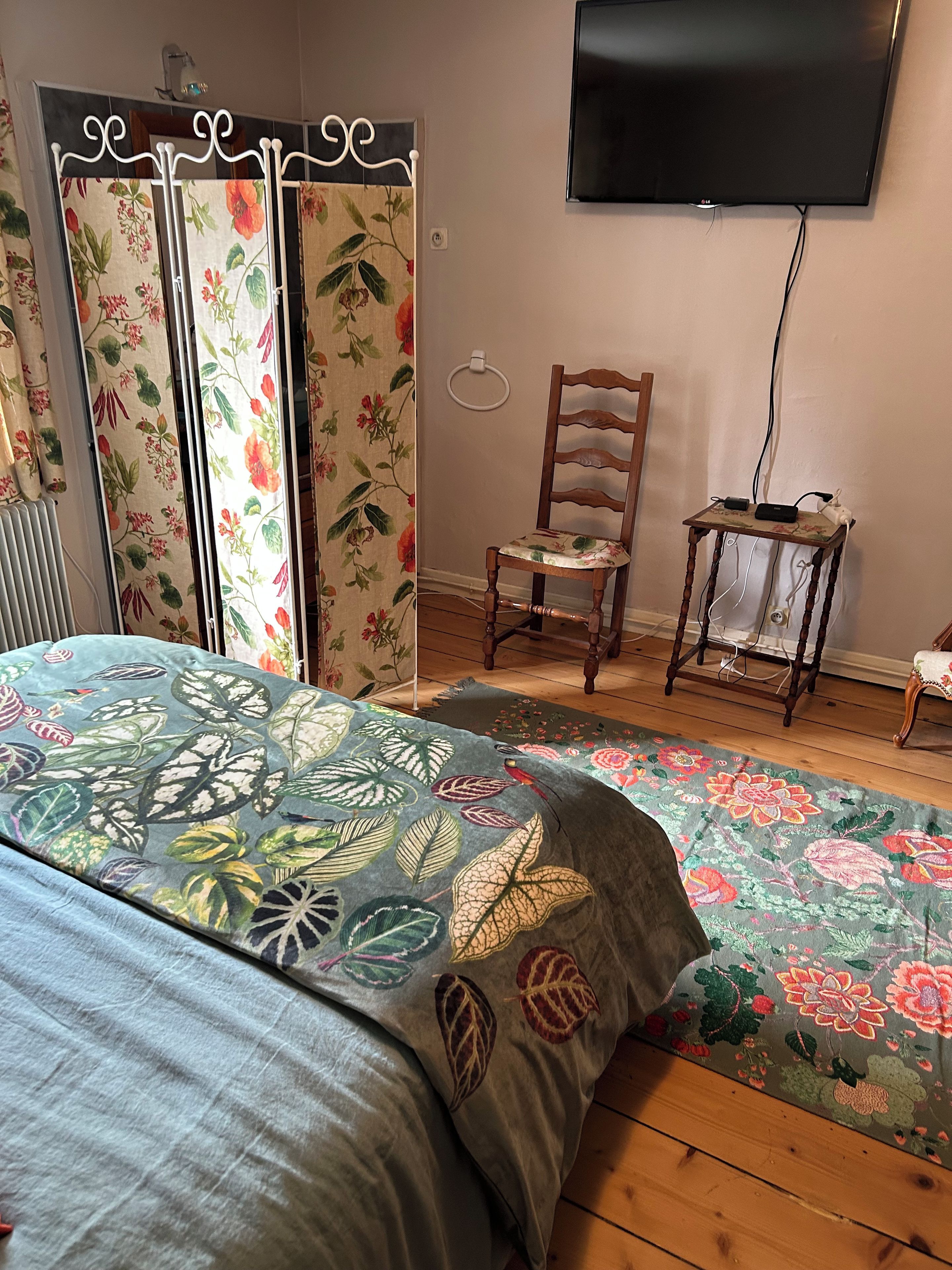 Un dormitorio con una cama, una silla, una mesita, un radiador y un televisor en la pared.