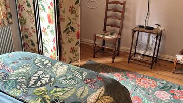 Un dormitorio con una cama, una silla, una mesita, un radiador y un televisor en la pared.