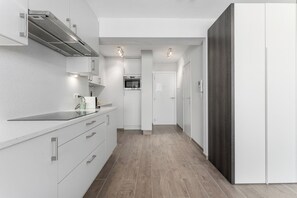 A modern kitchen with white cabinetry, a built-in oven, and a stainless steel range hood. - Blankenberge Beachfront Stay (BLANKENBERGE)