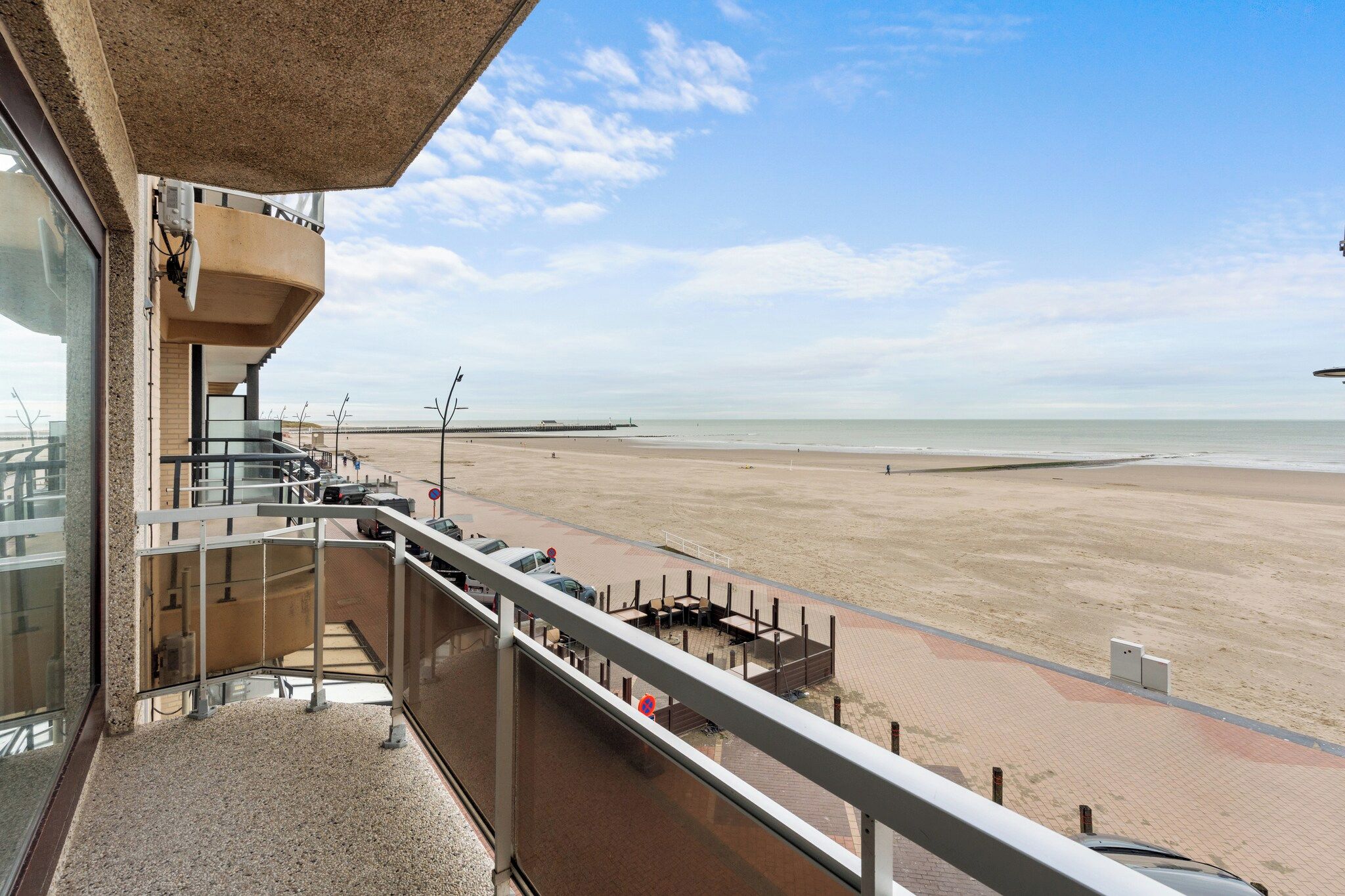 Un balcón con vistas a una playa, un estacionamiento y un edificio de techo plano.