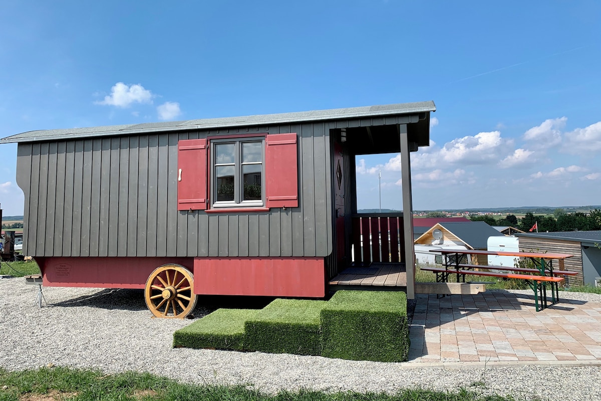 A small cabin with a window and a door, a wheel, and a picnic table.