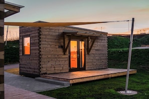 A small wooden cabin with a glass door, a wooden deck, and a metal pole. - Freizeitparadies Mohrenhof (Geslau)