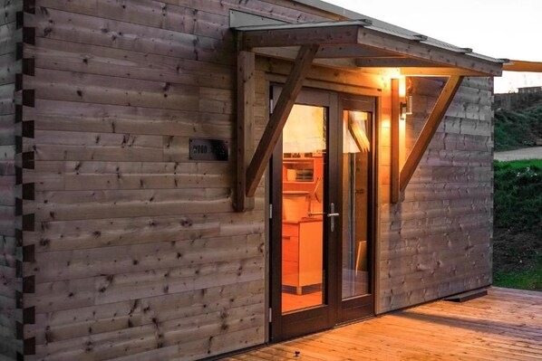 A wooden cabin with a glass door entrance, a wooden deck, and a small kitchen visible inside. - Freizeitparadies Mohrenhof (Geslau)
