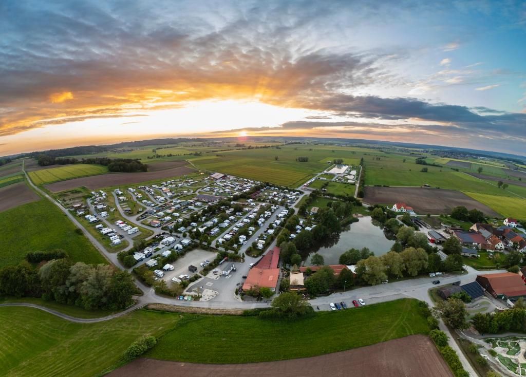 Eine Vogelperspektive zeigt einen Campingplatz mit mehreren Wohnmobilen und Wohnwagen, umgeben von grünen Feldern und einem kleinen Gewässer.
