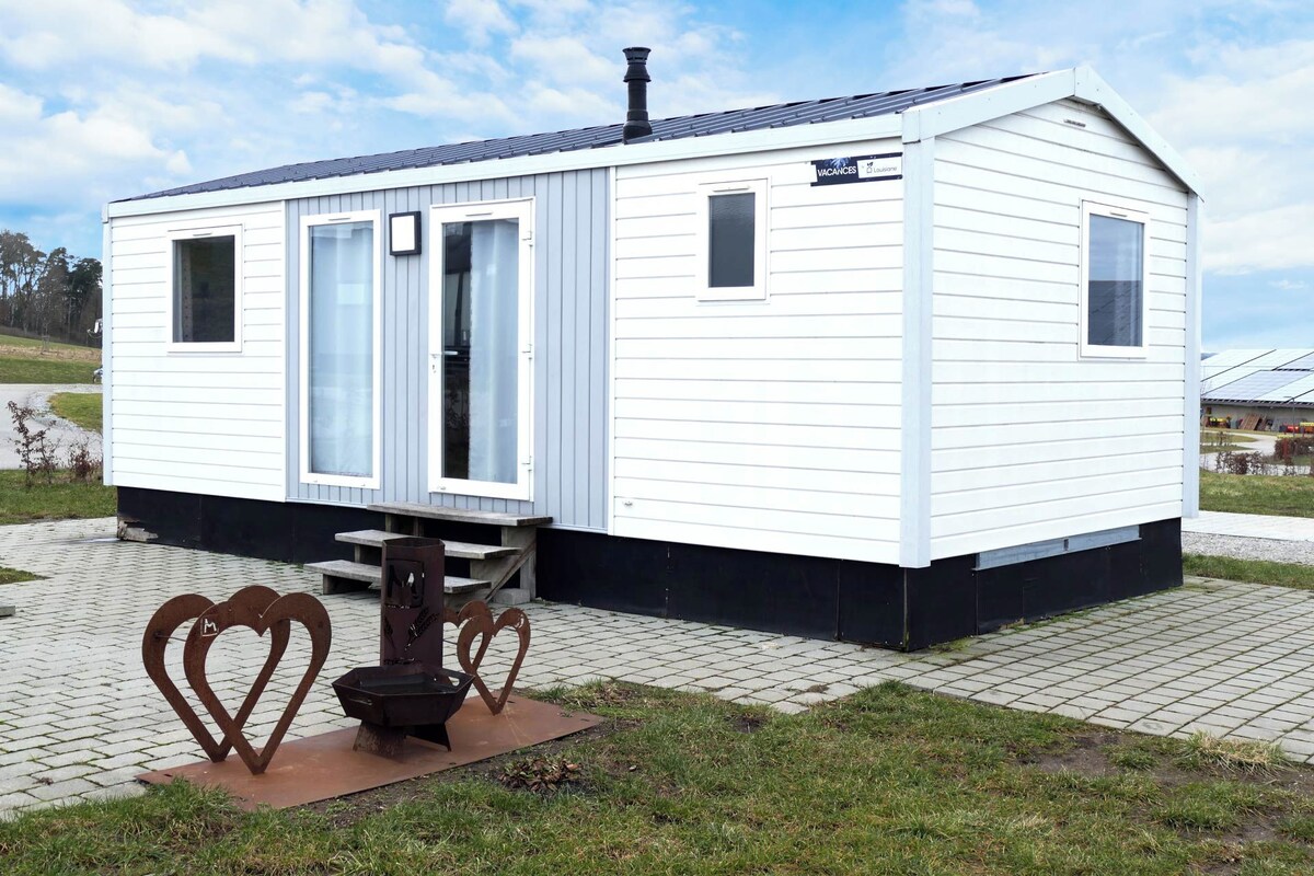 A small, single-story mobile home with a flat roof, a chimney, and a sign indicating availability for rent.