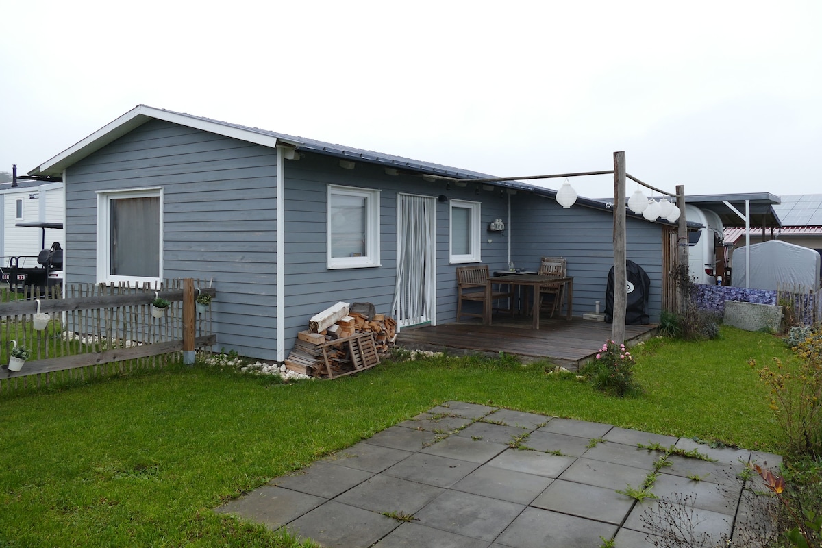 A single-story house with a covered porch, a fenced yard, and a stack of firewood.