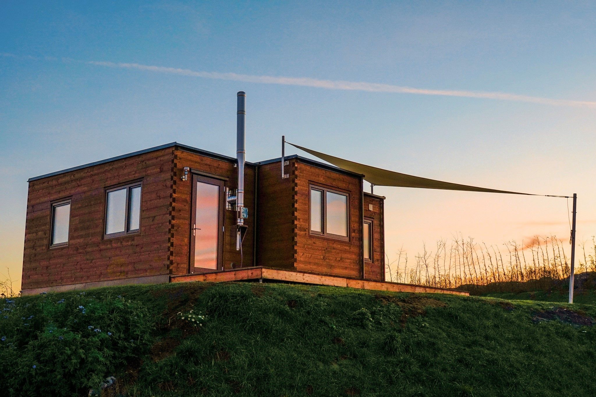 Eine moderne, zweigeschossige Holzhütte mit geneigtem Dach, großen Fenstern und einem sichtbaren Schornstein.
