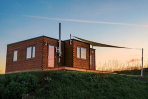 A modern, two-story wooden cabin with a sloped roof, large windows, and a visible chimney.