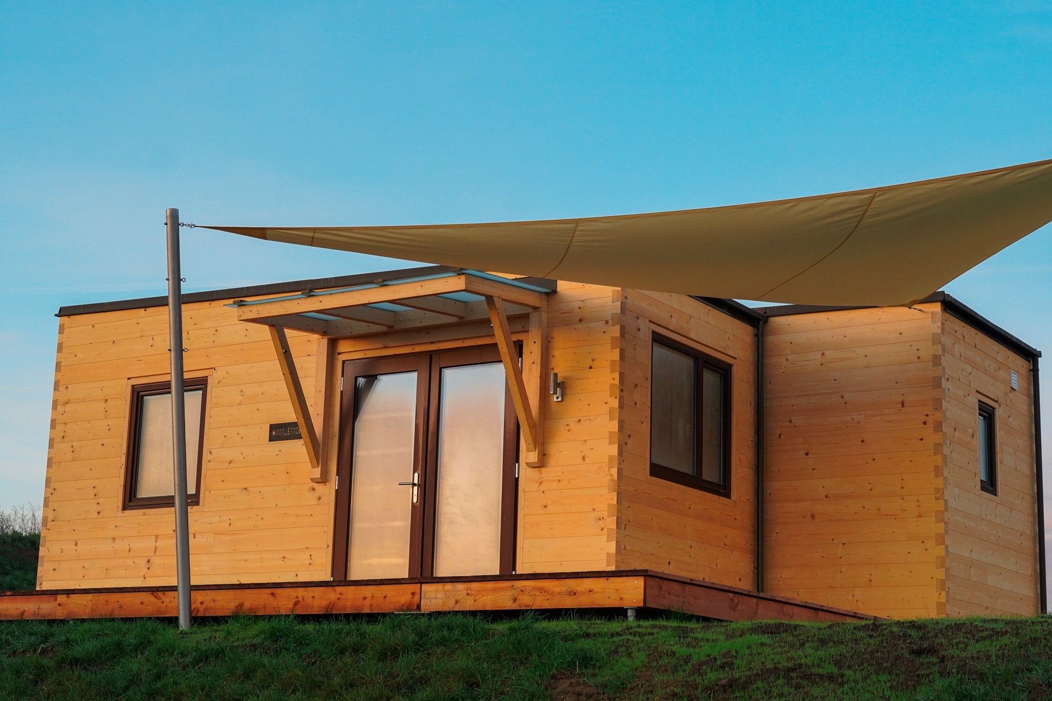 A wooden cabin with a large window, a door, and a covered patio area.
