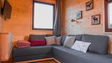 Una habitación acogedora con un sofá seccional gris, una pared de madera con ilustraciones de animales y una ventana con cortina.