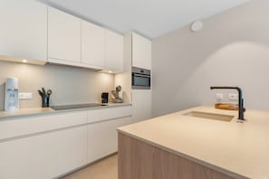 Une cuisine moderne avec des meubles blancs, un four encastré, une machine à café et un évier avec un robinet.