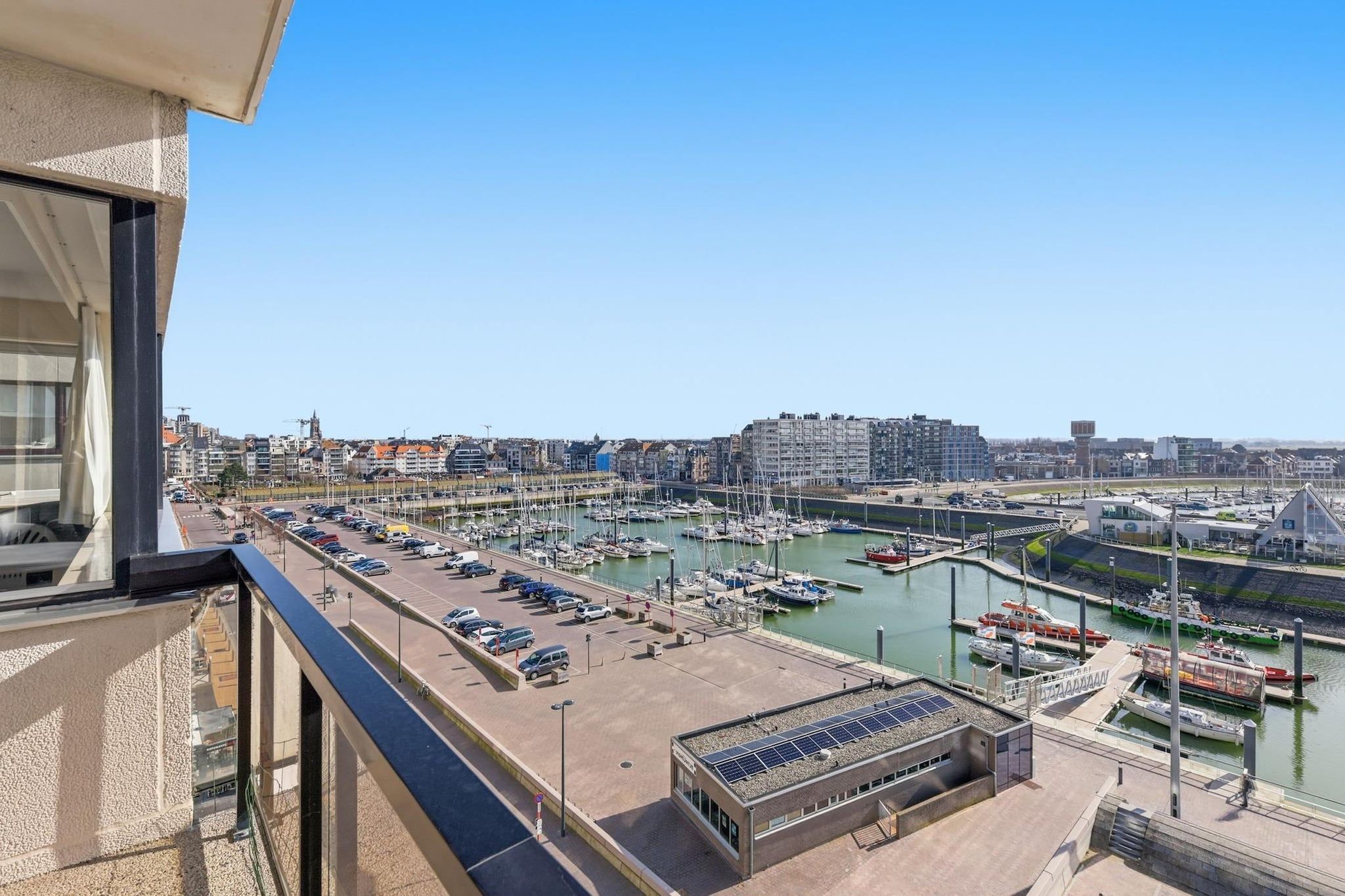 Un port de plaisance avec des bateaux amarrés, un espace de stationnement et des bâtiments en arrière-plan.