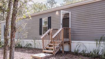 A single-story mobile home with a wooden staircase leading to a front door.
