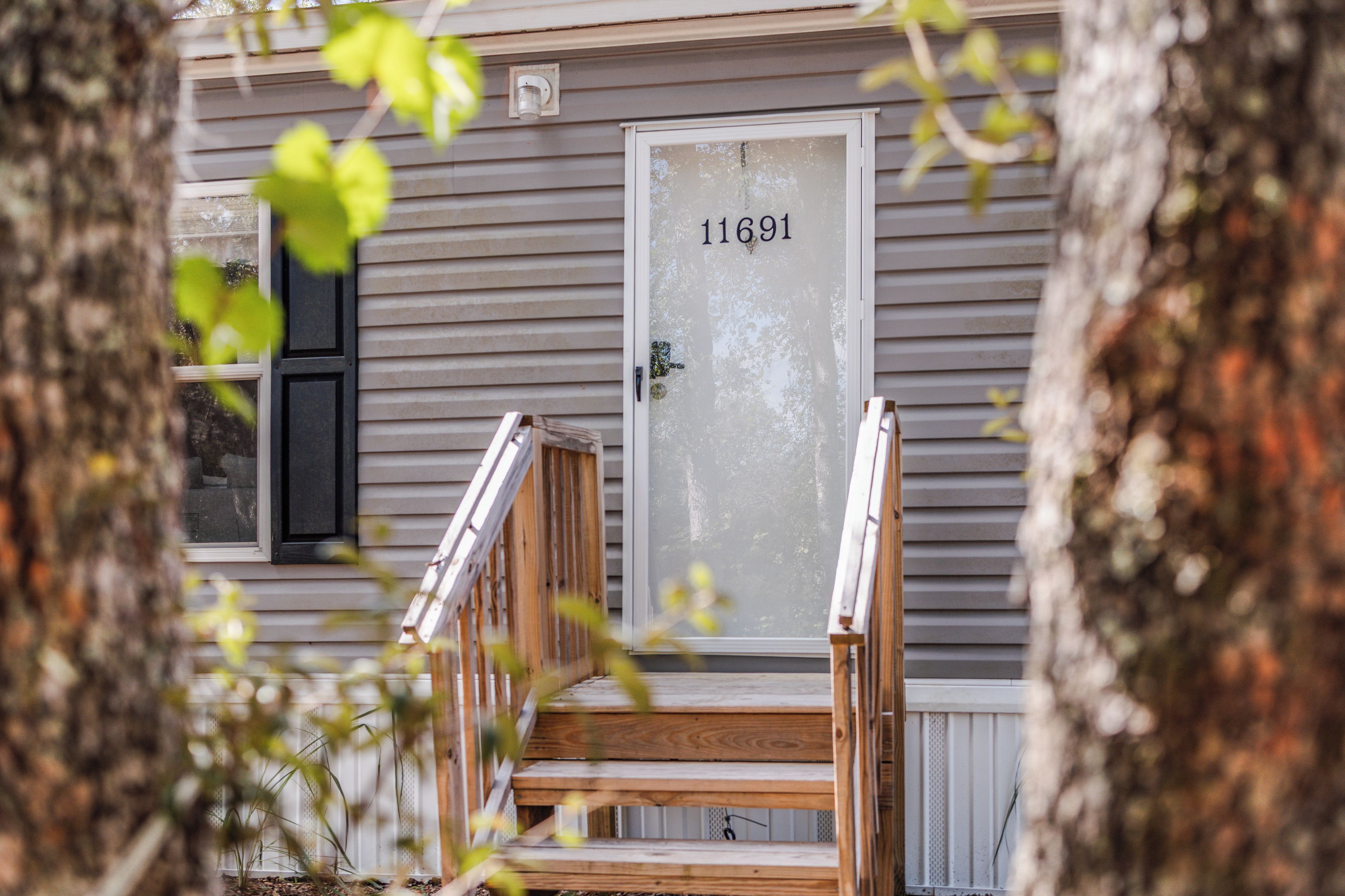 A house with a wooden front porch, a white door with the number 11691, and a window with blinds.