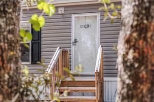 Una casa con un porche de madera, una puerta blanca con el número 11691 y una ventana con persianas.