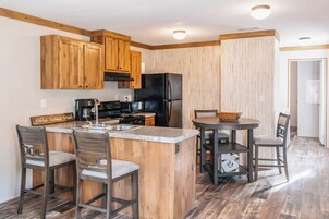 Cocina moderna con gabinetes de madera, refrigerador negro, cafetera y comedor con mesa y sillas.