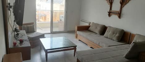 A living room with a sofa, a coffee table, a TV, and a wall-mounted shelf.