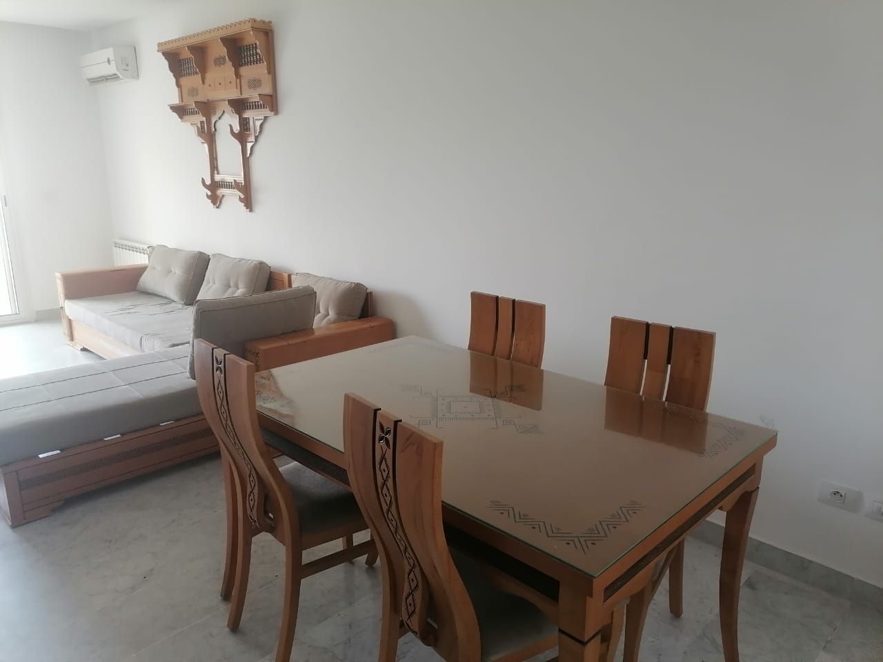 En matplats med ett bord med glasskiva och trästolar, en soffa och en dekorativ väggdekoration.