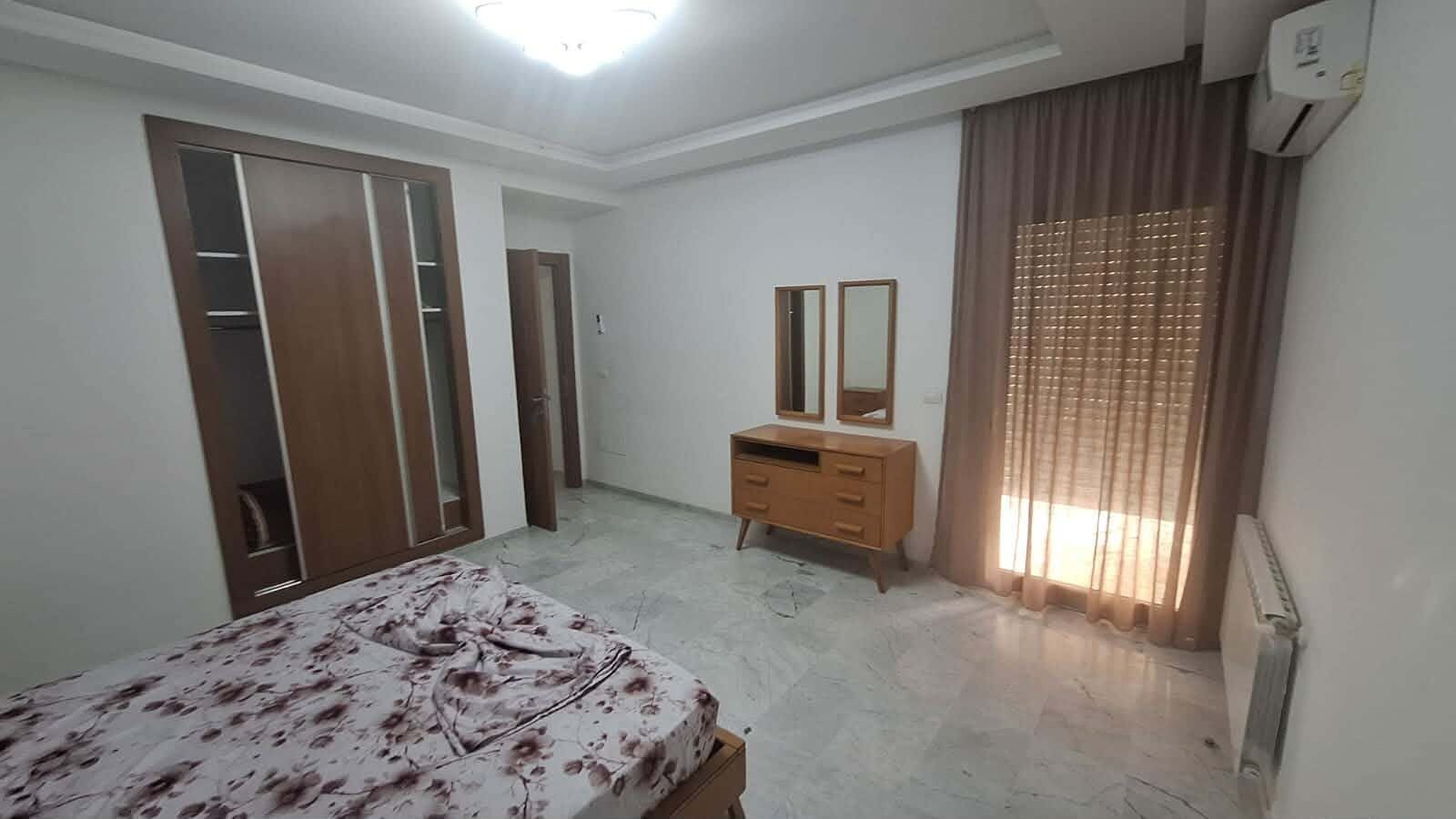 A bedroom with a bed, a dresser, a wardrobe, and a window with curtains.