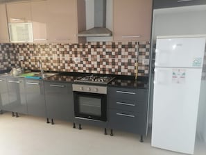 A kitchen with a gas stove, oven, and a white refrigerator. - Fully Furnished Two-Bedroom Apartment in Khezama – Prime Location (Sousse)