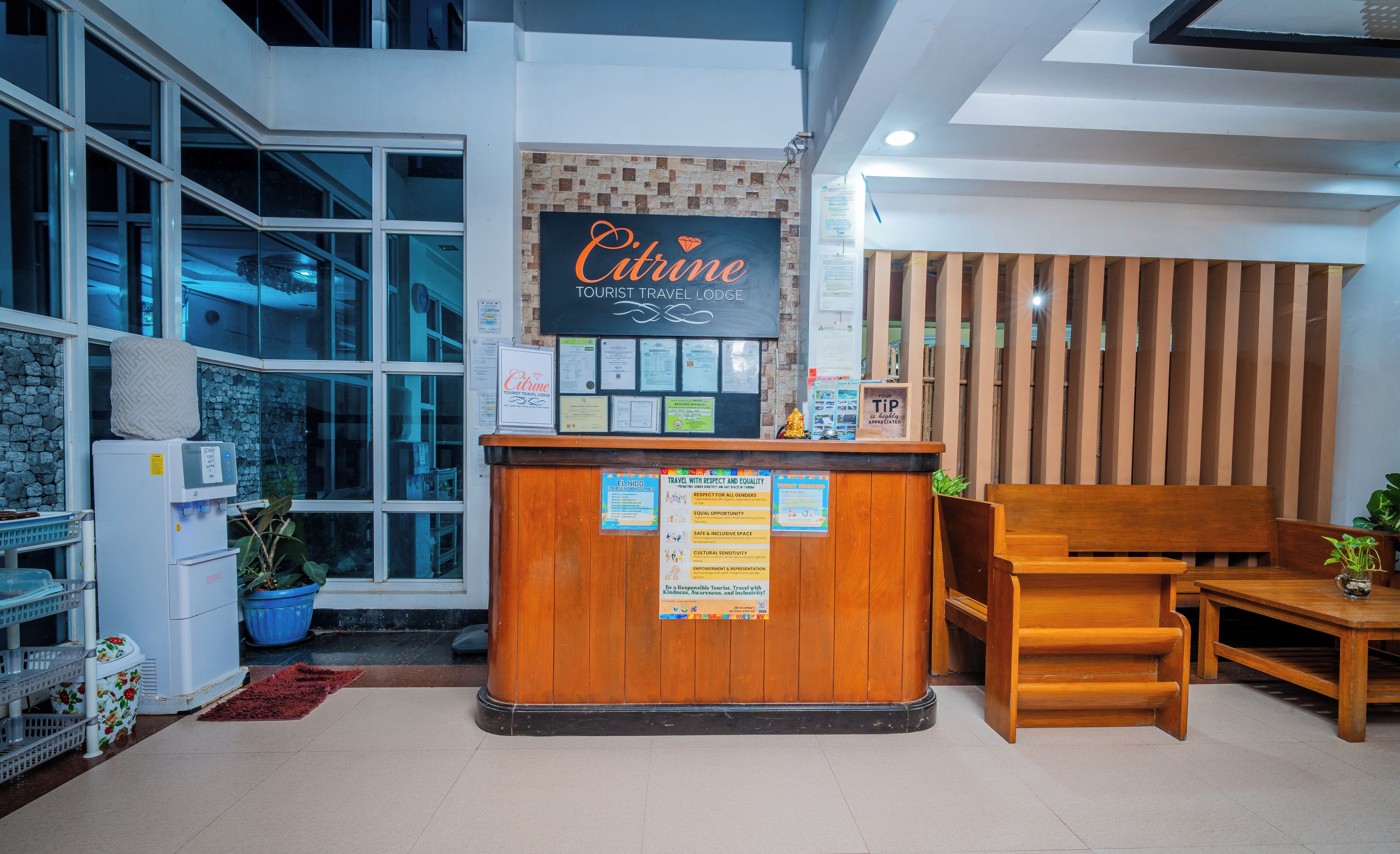 En receptionsdisk med en skylt som visar texten ”Citrine Tourist Travel Lodge” och informationsaffischer på väggen.