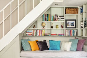 Eine Treppe führt zu einem Schlafzimmer im Dachgeschoss, das voll mit Büchern steht, mit einem Bett und bunten Kissen.