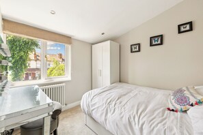 A bedroom with a bed, a desk, a radiator, and a window with a view of houses.