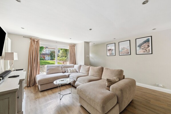 A modern living room with a sectional sofa, a coffee table, and a view of a garden through large windows.
