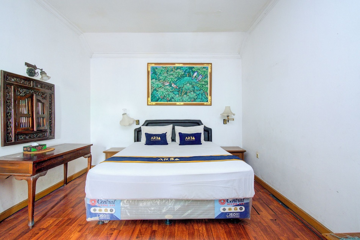 A hotel room with a bed, a painting on the wall, a desk, and a nightstand.