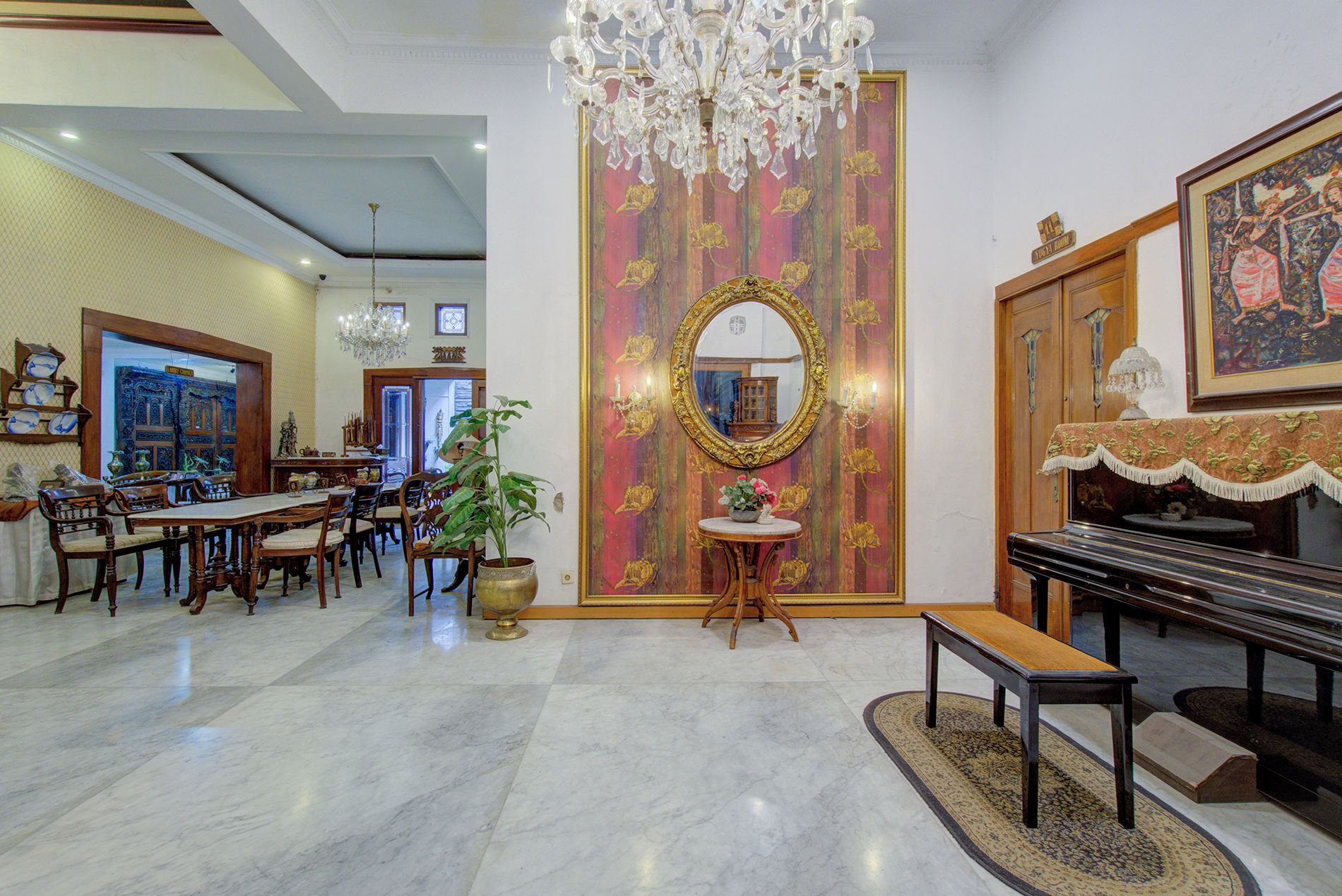 Un hall d’hôtel agrémenté d’un grand piano, d’un lustre, d’un grand miroir et d’un espace repas avec des meubles en bois.