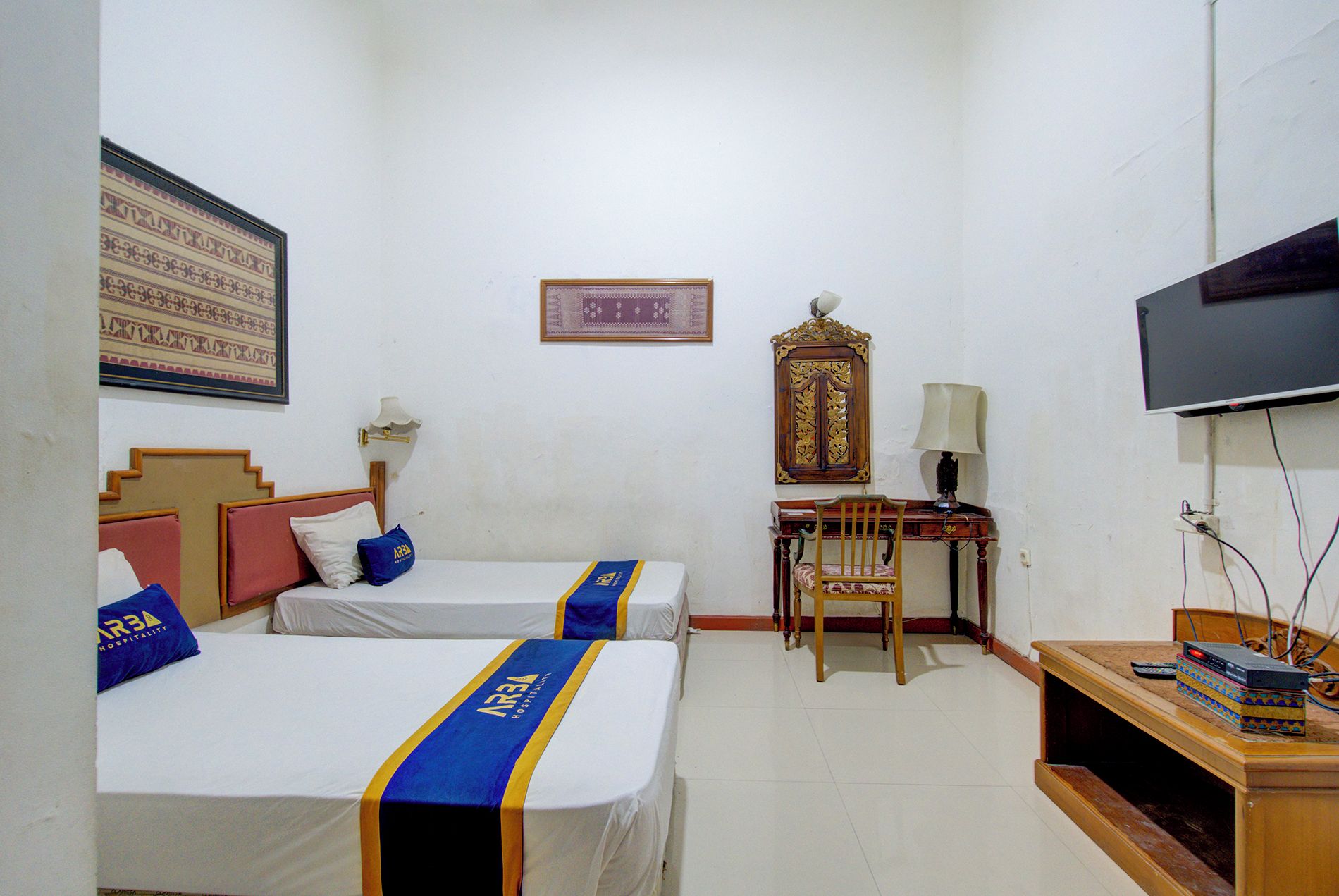 A hotel room with two beds, a desk, a television, and a wall-mounted decorative piece.