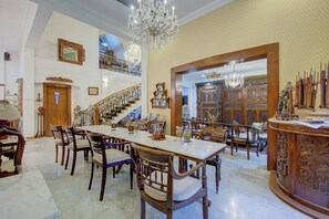 Un comedor espacioso con una mesa de mármol y sillas de madera, un candelabro y una escalera que lleva a un nivel superior.