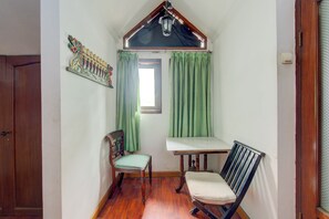 Una habitación con techo inclinado, una ventana con cortinas verdes, un banco de madera y una silla.