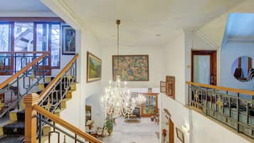 Una imponente escalera con barandales decorativos que conduce a un rellano con una araña y obras de arte.
