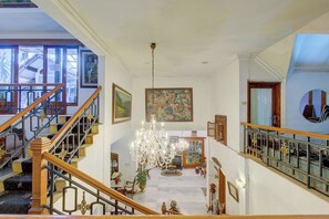 Una imponente escalera con barandales decorativos que conduce a un rellano con una araña y obras de arte.
