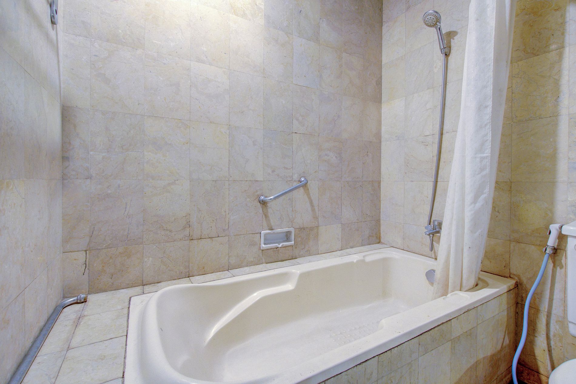 A bathroom with a bathtub, a showerhead, and a handrail.