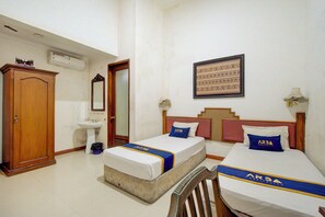 A hotel room with two beds, a wooden wardrobe, a sink, and a framed picture on the wall.
