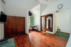 A hallway with wooden flooring, a television, a chair, and a door with a mirror. - ETHNIC Hotel By CQA (Bandung)