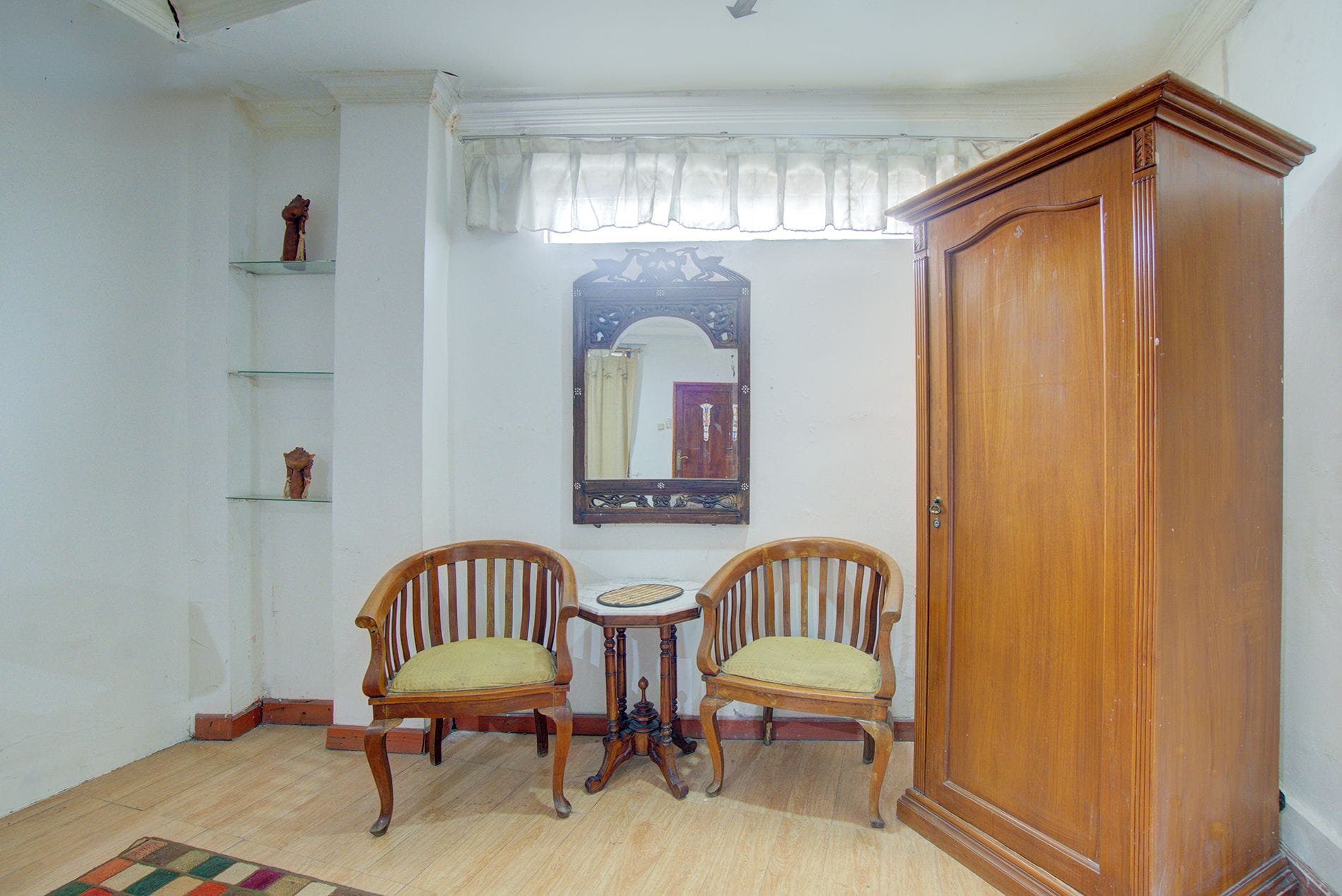 Une pièce comprenant deux chaises en bois, une petite table, un meuble et un miroir fixé au mur.