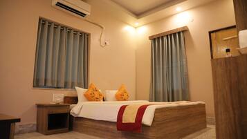 A bedroom with a wooden bed, two nightstands, a wall-mounted air conditioner, and a window with curtains.