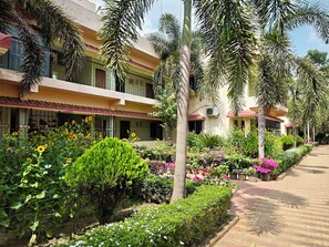 Un hotel con varios pisos, balcones y un jardín con plantas y flores diversas.